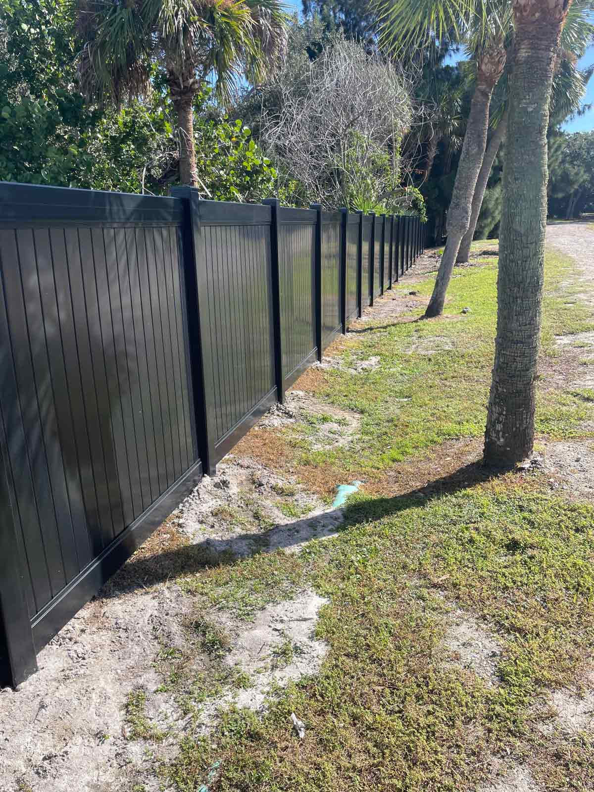 Solid vertical black vinyl fence along gravel road
