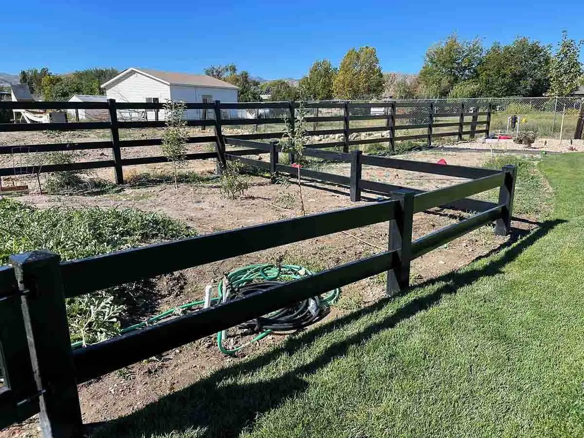 Black vinyl 2 rail ranch fence installed around a garden area