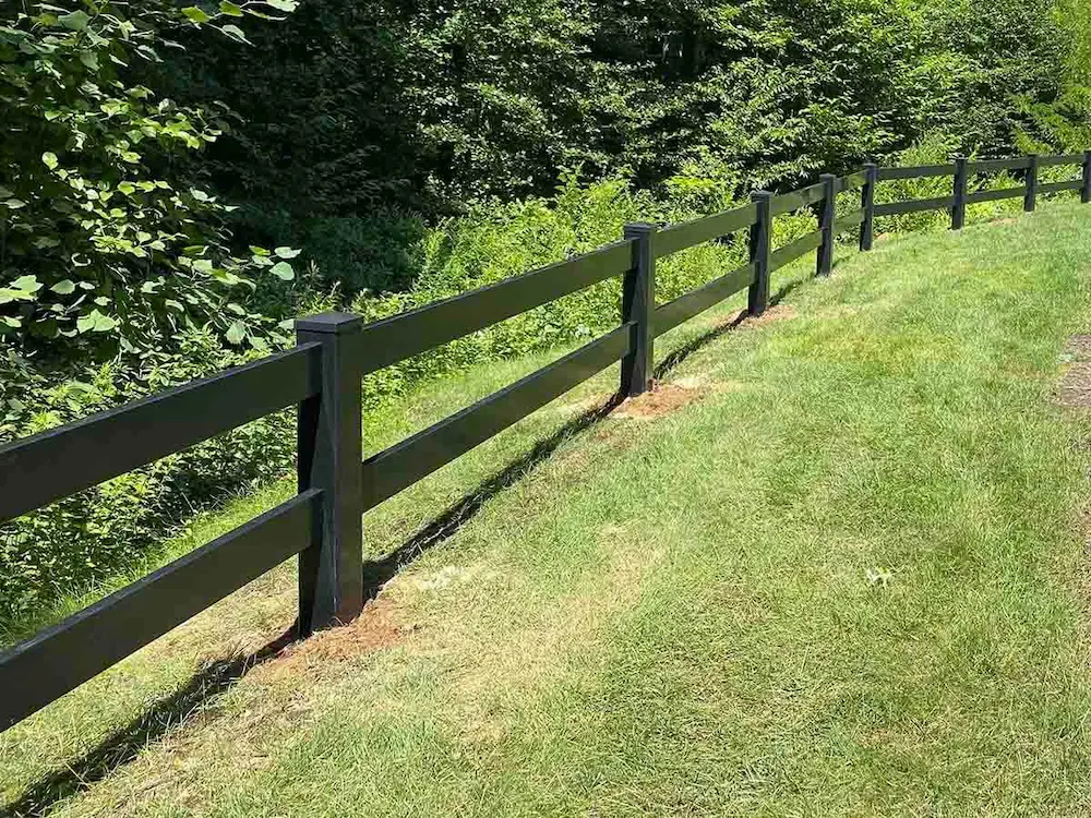 Black 2 rail vinyl ranch rail fence bordering a wooded area