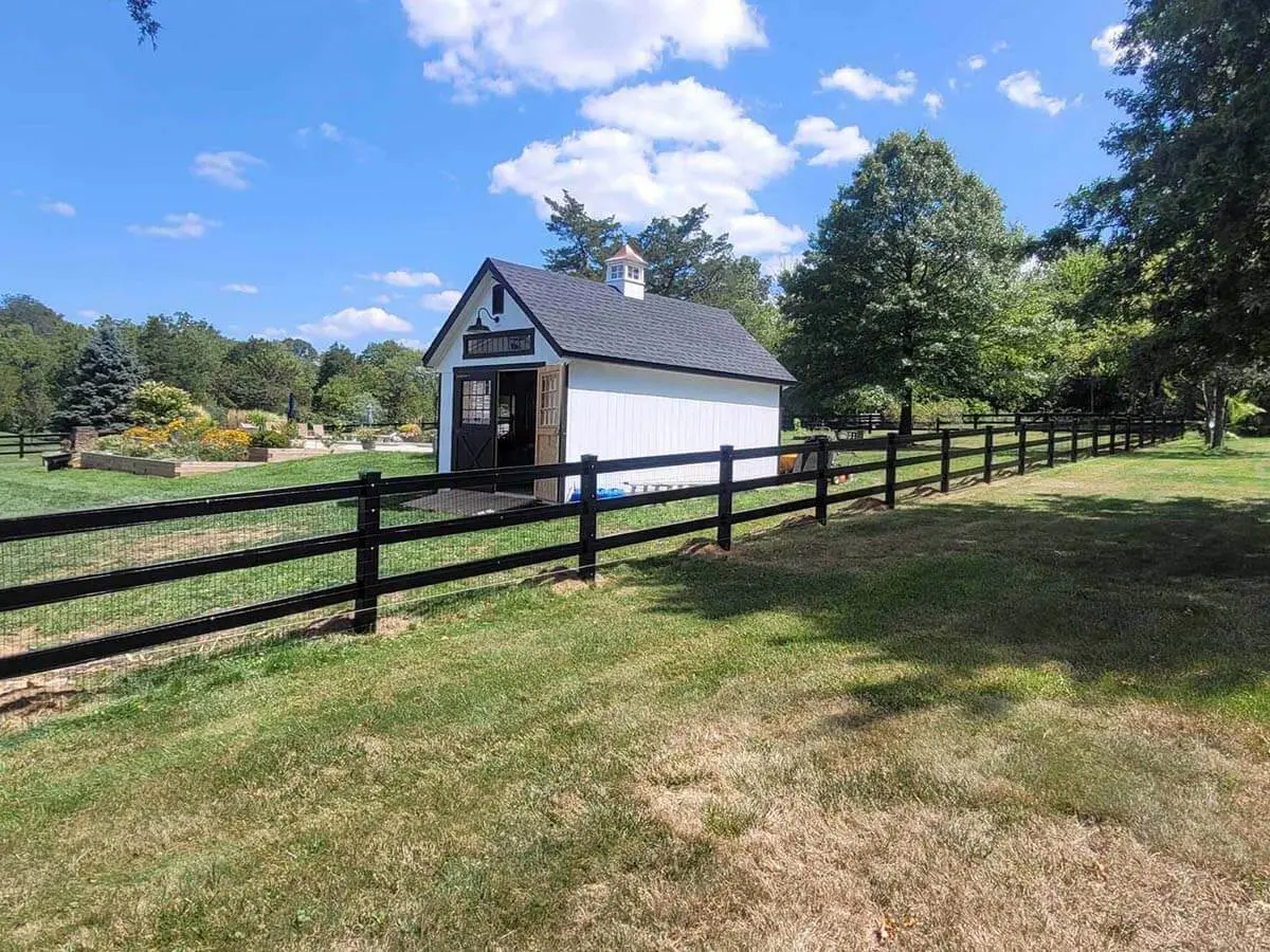 Black vinyl 3 rail ranch fence with wire mesh installed around a shed