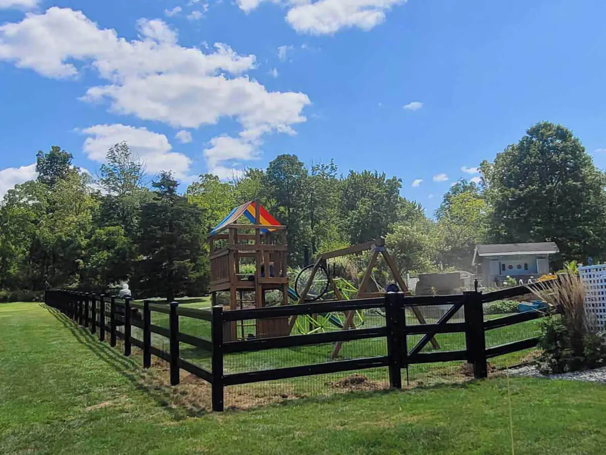3 rail black vinyl fence with wire mesh installed around a backyard playground