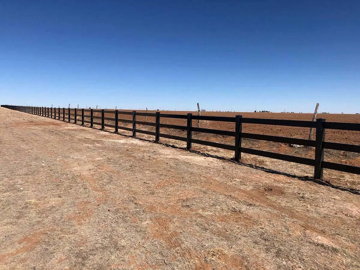 Black vinyl 3 rail ranch fence installed around a dirt pasture