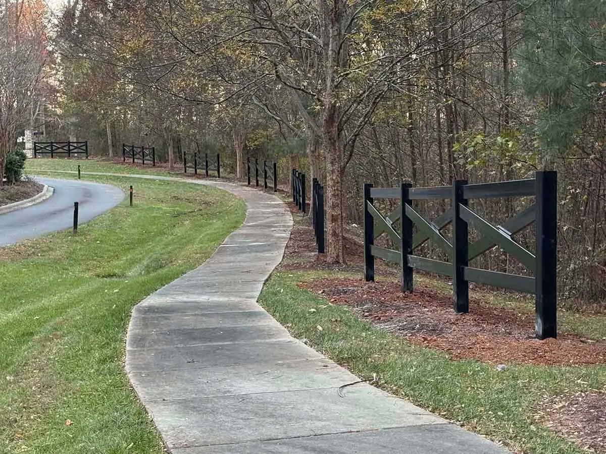 Crossbuck black vinyl ranch fence installed along a sidewalk next to a road