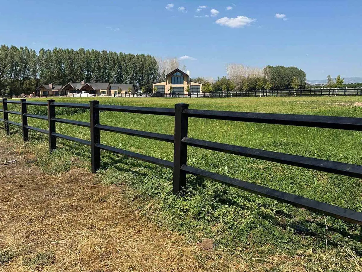 Diamond rail black vinyl horse fence installed around a horse pasture with a barn