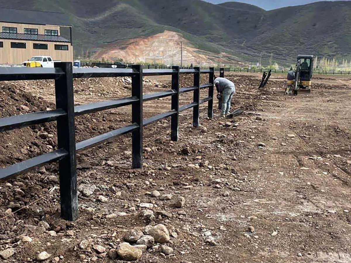 Diamond rail black vinyl fence installed on a farm property with a dirt pasture