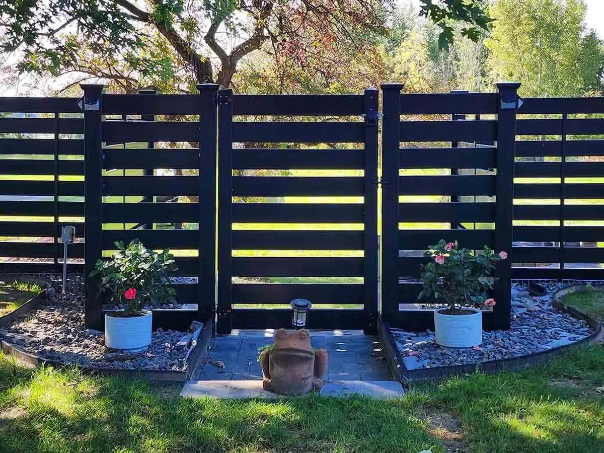 Horizontal semi-privacy black vinyl fence and gate installed around a grass yard