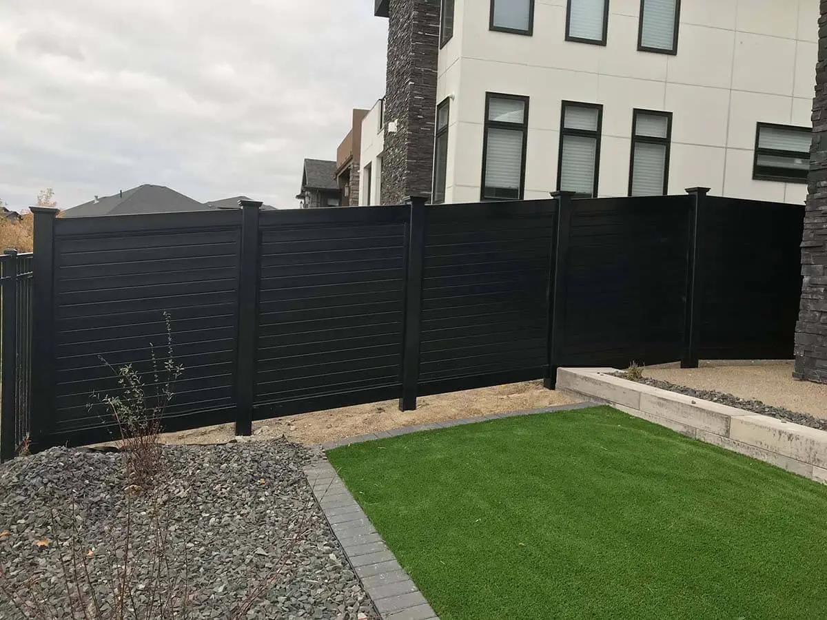 Horizontal solid privacy black vinyl fence installed on uneven ground