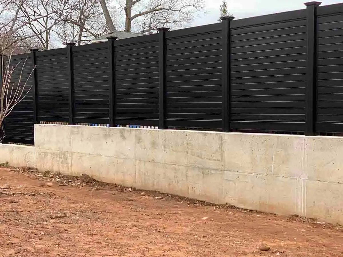 Horizontal privacy fence made of black vinyl installed on a concrete wall