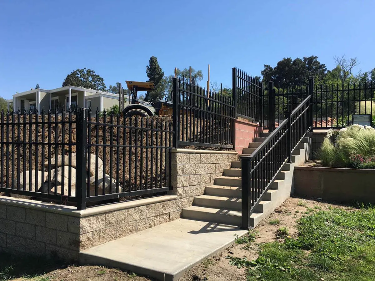 Black vinyl ornamental railings installed along a staircase and on top of an uneven ground stone wal
