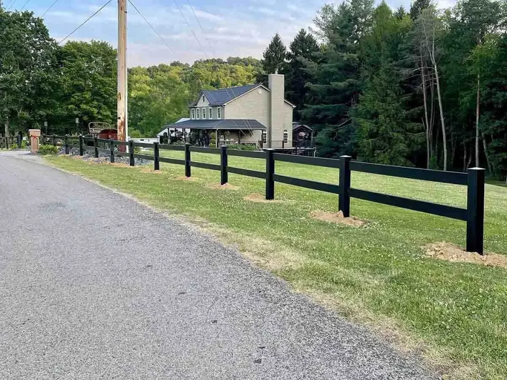 Black two-rail vinyl fence along a gravel road beside a lawn.