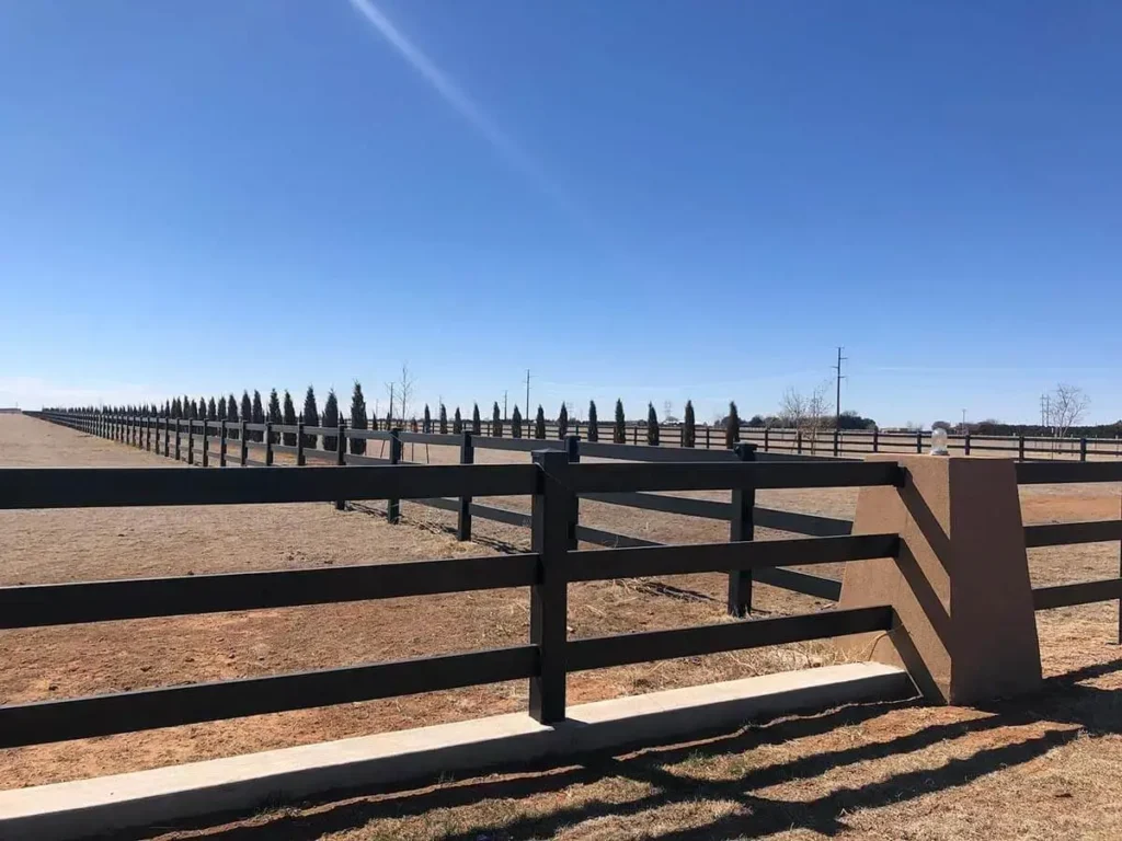 Black three-rail vinyl fence around a dry pasture.