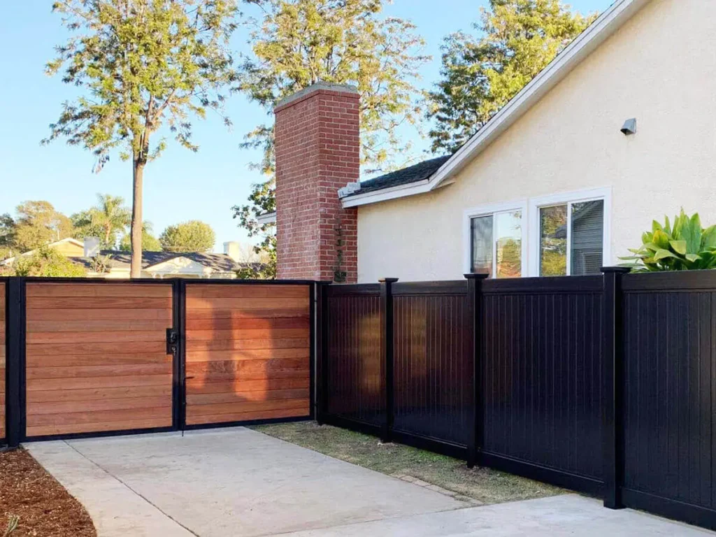 Black privacy fence beside a wood-tone double gate and house.